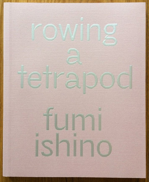 The photography book cover of Rowing in a Tetrapod by Fumi Ishino. Hardback pink cover with silver text.