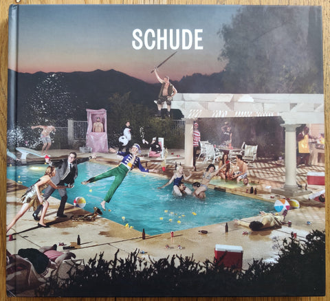 The photography book cover of Schude by Ryan Schude. hardback with image of people at a party jumping into a big pool.