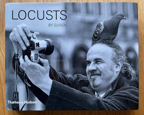 The photography book cover of Locusts by Sasha Gusov. Hardback with B&W photograph of a man taking a picture of himself with a pigeon on his head.