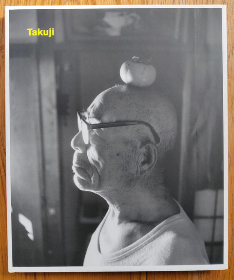 The photography book cover of Takuji by Shingo Wakagi. Hardback in yellow with cover in B&W of a man with a piece of fruit on his head.