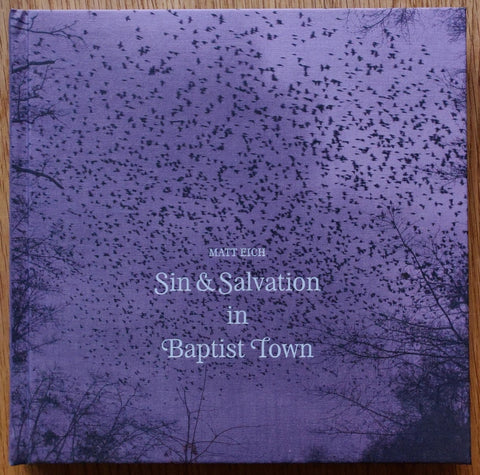 The photography book cover of Sin & Savation in Baptist Town. Hardback purple cover with image of a collection of birds in the sky.