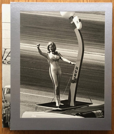 The photography book cover of Nitro by Steve Banks. Hardback with image of a woman standing on a platform in an all-in-one zipped suit.