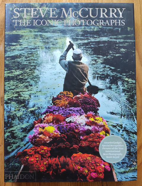 The photobook cover of The Iconic Photographs by Steve McCurry. In dust jacketed hardcover black.
