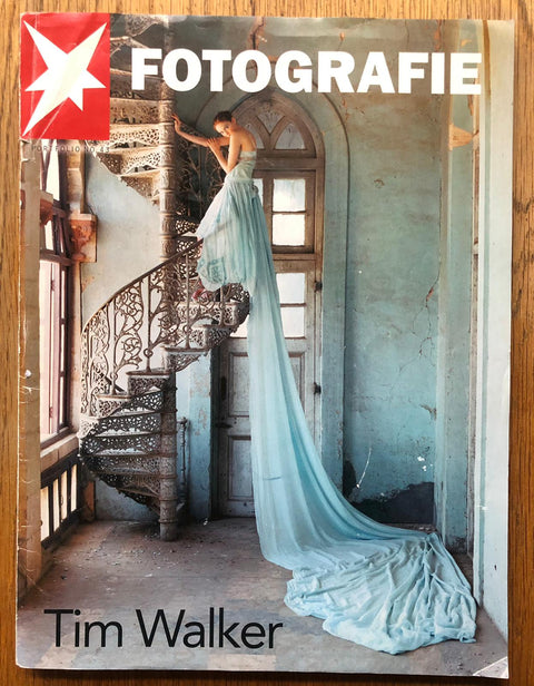 The photography book cover of Fotografie by Tim Walker. Paperback magazine with image of a woman in a long blue dress standing on a spiral staircase.
