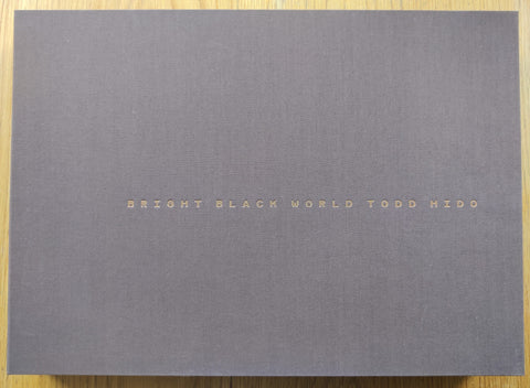 The photobook cover of Bright Black World by Todd Hido. Hardcover clamshell box in grey/purple with centered title. Signed.
