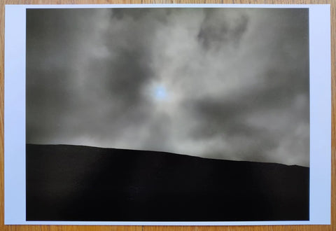 The photography book cover of Bright Black World by Todd Hido. Hardback with image of landscape and sun through the clouds.