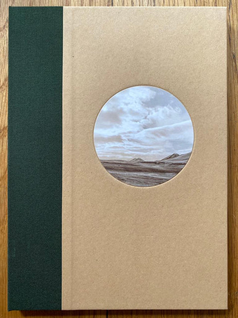 The photography book cover of Untitled #11856-0820 by Todd Hido. Hardback in beige with dark green spine and circle photograph of mountains/sky. Signed.