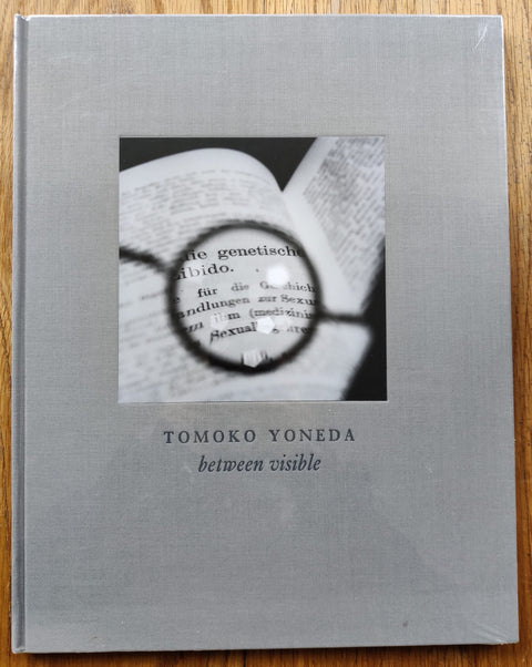 The photography book cover of Between Visible by Tomoko Yoneda. Hardback in light grey.