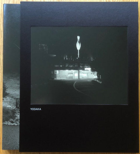 The photography book cover of Yodaka by Toshio Shibata. Hardback slipcase cover in black with building lit up in the dark.