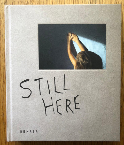 The photography book cover of Still Here by Vivian Rutsch. Hardback in light grey with photo of a child holding their hands up to a wall.