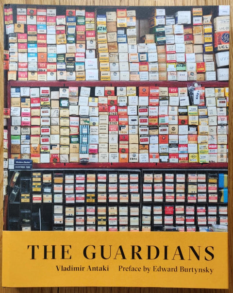 The photography book cover of The Guardians by Vladimir Antaki. Hardback with yellow bellyband, and image of shop shelves on the cover.