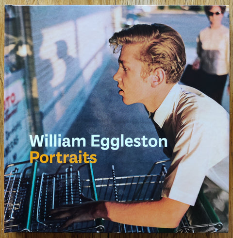 The photography book cover of Portraits by William Eggleston. Hardback with image of a man pushing trolleys on the cover.