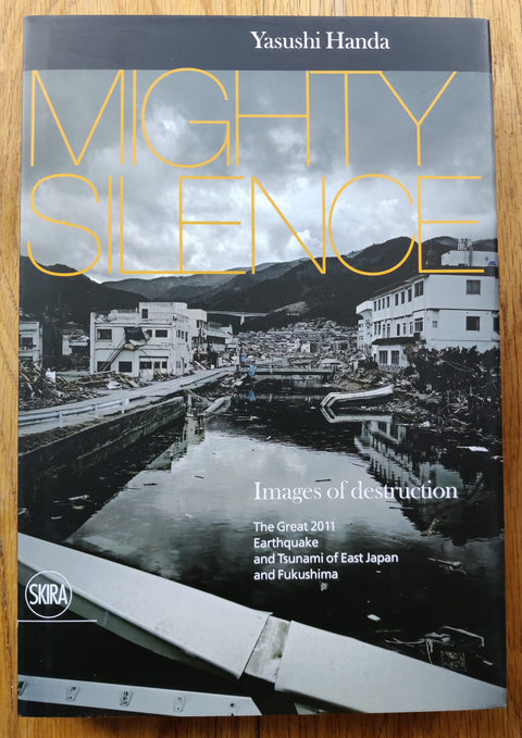 The photography book cover of Mighty Silence: Images of Destruction by Yasushi Handa. Hardback in B&W with yellow title.
