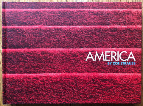 The photography book cover of America by Zoe Strauss. Hardback in red with "AMERICA" title in white and author in blue.
